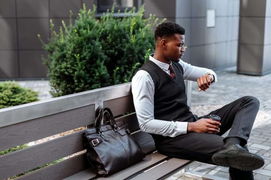 Young professional sitting on a bench, checking his wristwatch with coffee in hand.