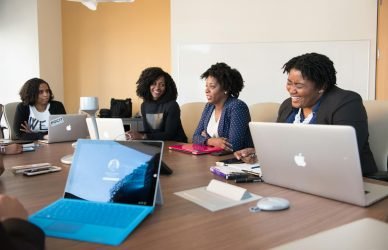 Group of women engaged in a collaborative meeting at an office table with laptops.